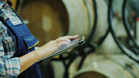 Hands-Of-A-Worker-With-A-Tablet-On-A-Background-Of-Wine-Barrels-Works-In-The-Winery