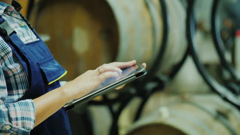 hands of a worker with a tablet on a background of wine barrels works in the winery