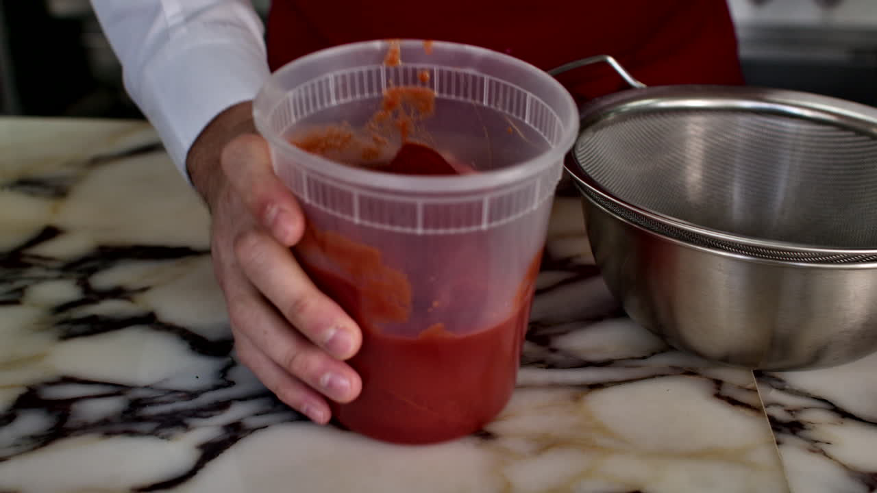 Close-up of a chef's hands holding a container of whole peeled tomatoes next to a sieve in a generic kitchen setting. Professional culinary ingredient preparation for a red sauce