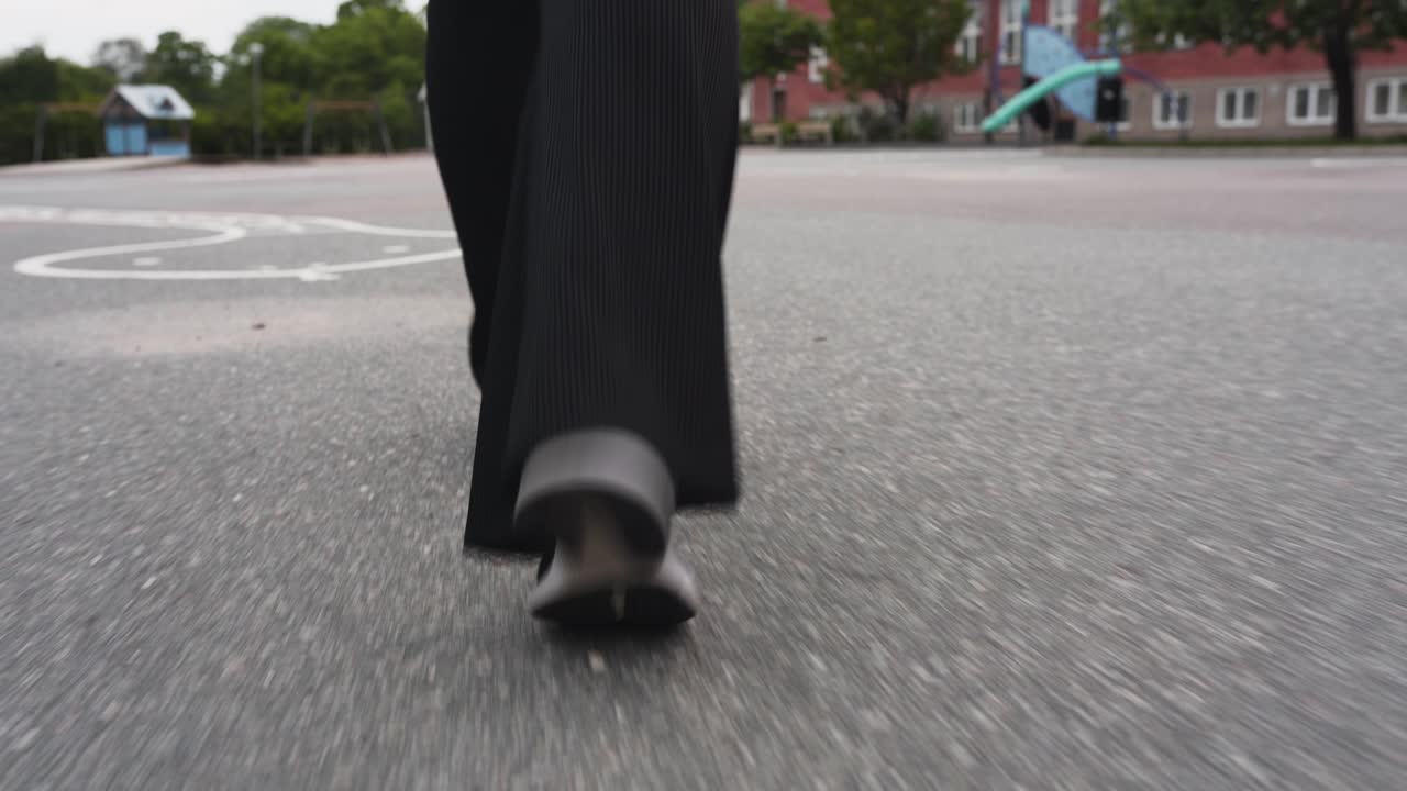 imágenes en movimiento de primer plano siguiendo los pies de una mujer caminando en el patio de una escuela sobre asfalto
