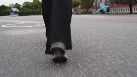 Imágenes-En-Movimiento-De-Primer-Plano-Siguiendo-Los-Pies-De-Una-Mujer-Caminando-En-El-Patio-De-Una-Escuela-Sobre-Asfalto