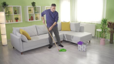 mature man mopping floor with mop in living room at home and getting tired.