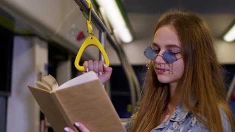 Portrait-of-attractive-young-adult-woman-stay-at-empty-subway-train-and-reading-interesting-book