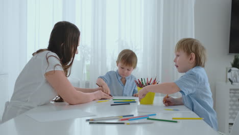 mom and her two sons sitting at the kitchen table drawing colored pencils family drawing on the lawn in the summer.