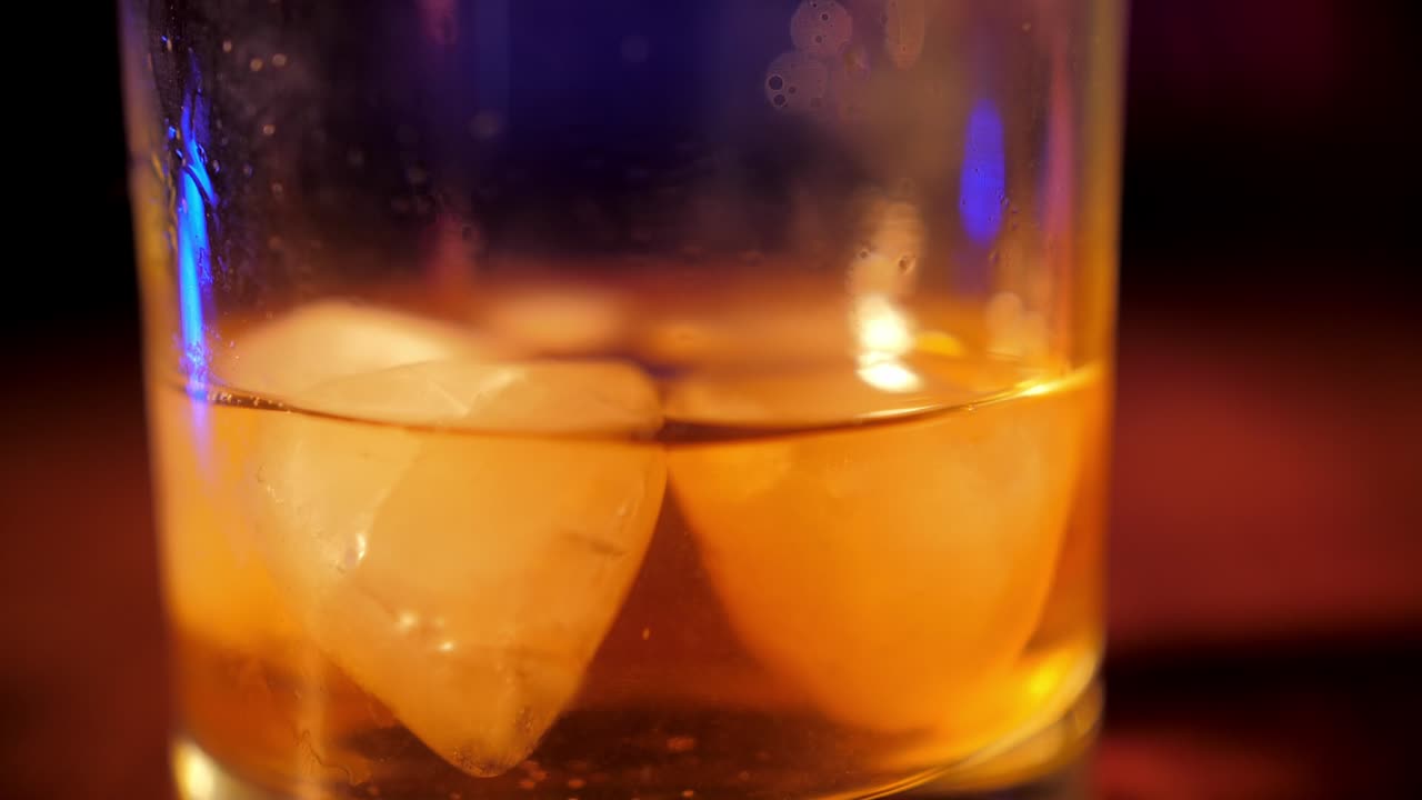 Primo piano di un bicchiere di whisky con ghiaccio su un bancone da bar