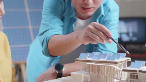 close up of asian man and woman helping each other building the model of a small house with solar panel