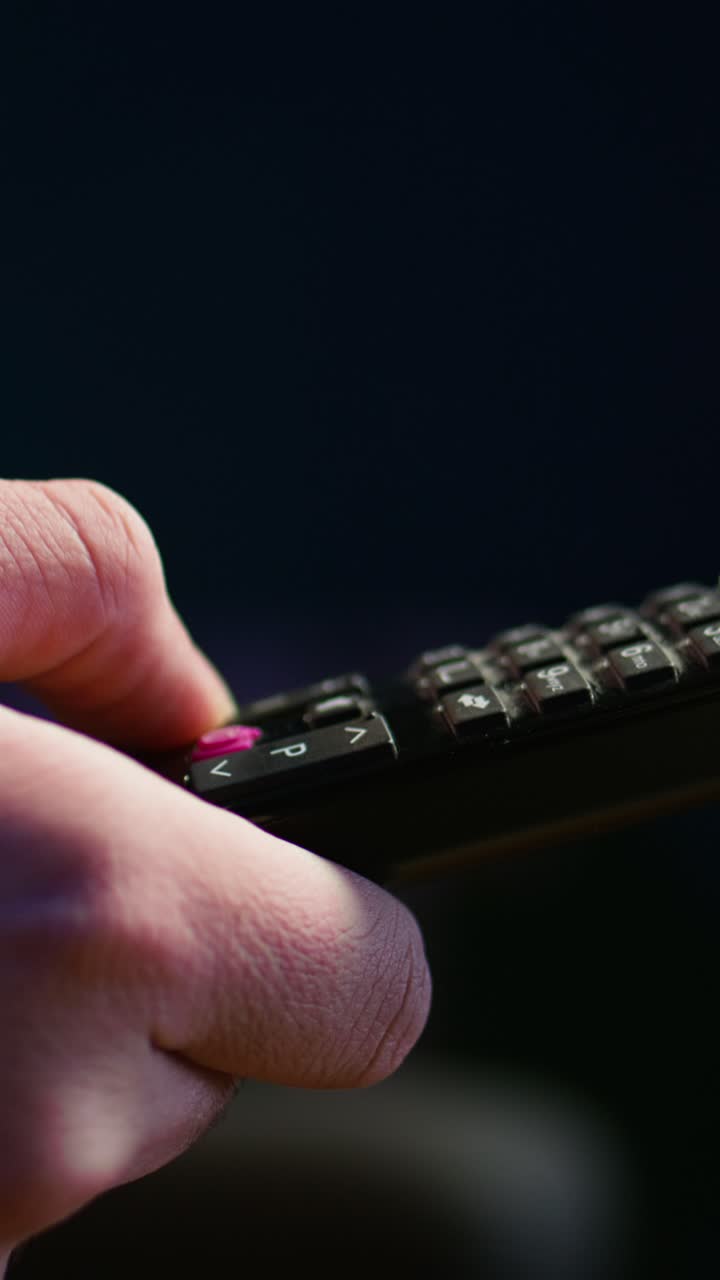 Vertical video Close up of man on couch using remote control flipping through channels on TV