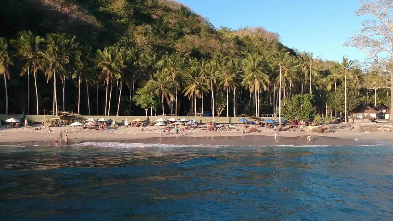 drone fly away from a small tropical beach paradise with palm tree and clear blue sky  in nusa penida indonesia