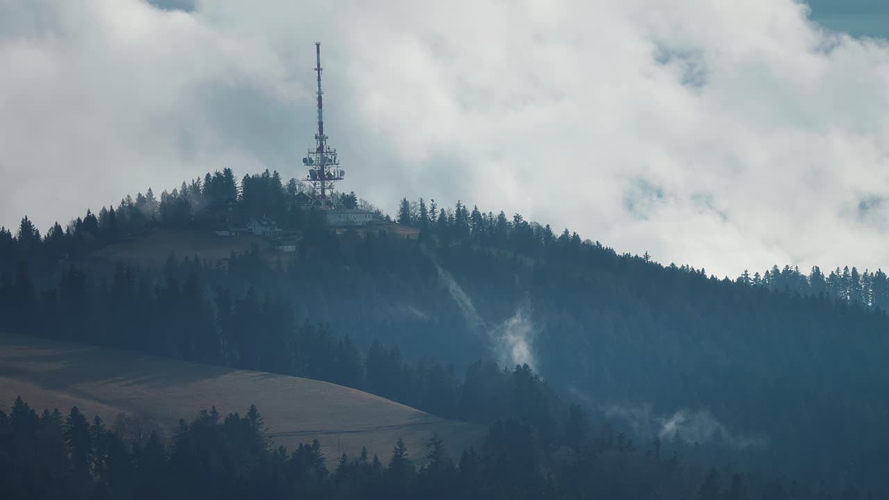 una torre de radiocomunicaciones con una multitud de antenas unidas se encuentra en la cima de la colina cubierta de bosque en los alpes austriacos