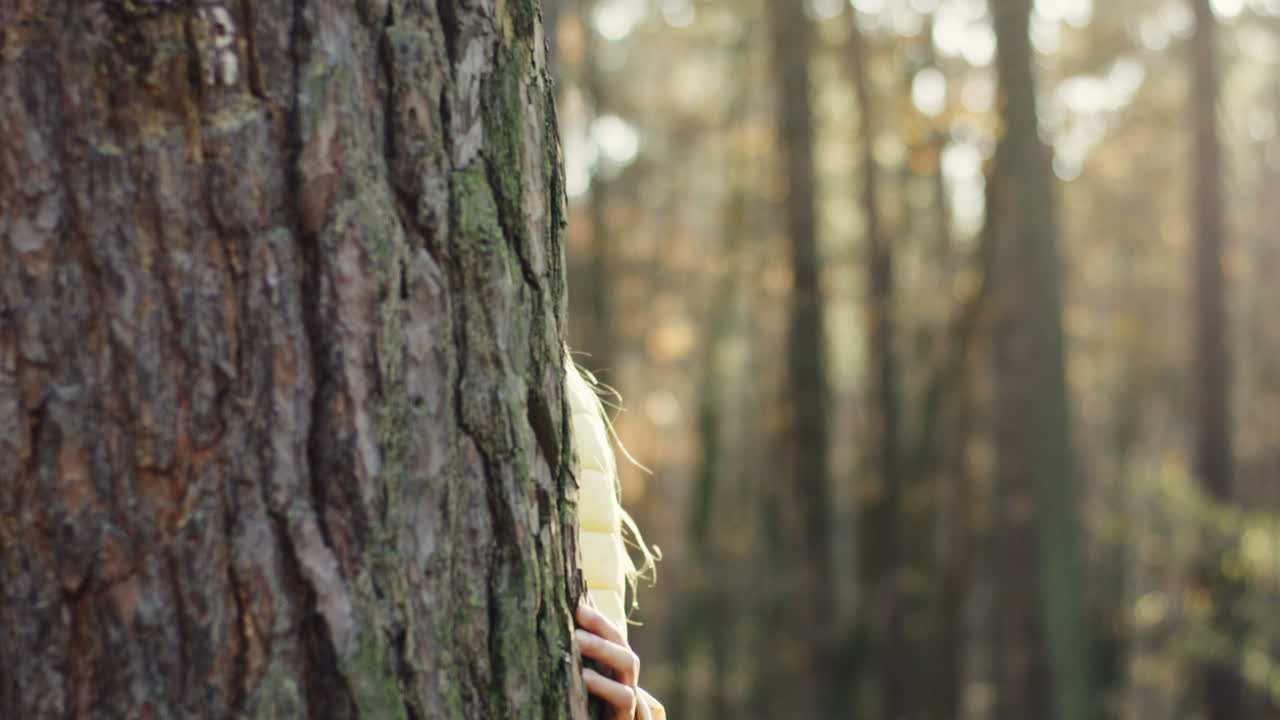 retrato de una adolescente caucásica mirando la cámara detrás de un tronco de árbol en el bosque