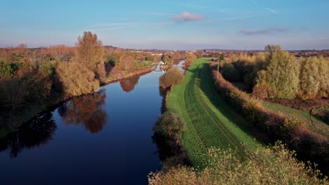 río que sigue fluyendo con espejo como reflejo del cielo, con camino de hierba, pasarela y árboles