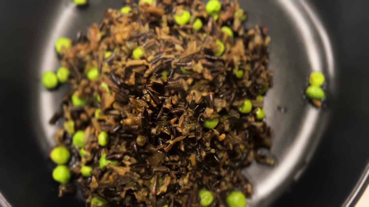 Close-up of steaming wild rice and green peas in a saucepan, hot plant-based food freshly cooked