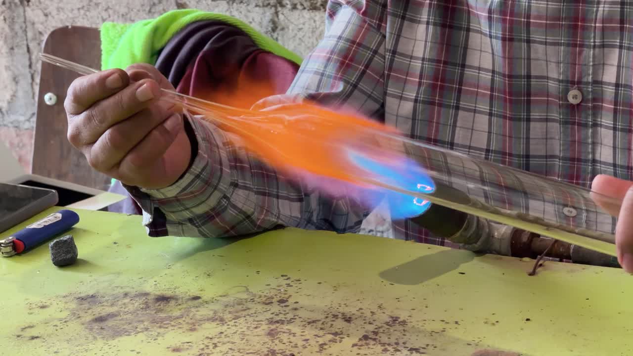 Filmato orizzontale di un artigiano esperto che modella vetro soffiato su una fiamma brillante.