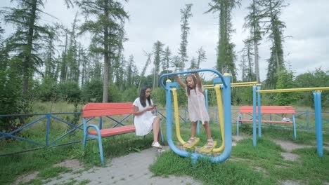 a pregnant mother and her young daughter enjoy playful time together at a playground in the park, surrounded by trees and greenery