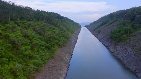 toma aérea hacia atrás de una pequeña presa de río rodeada de costa rocosa y plantas verdes que crecen en la colina