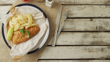 video of fish and chips on plate, salt and pepper and ketchup, with copy space on wooden table