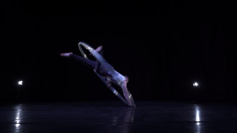 male muscular acrobat shows difficult tricks for a balance and concentration while spinning on a cyr wheel