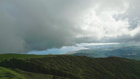 Clouds-hover-over-the-lush-green-hills-of-Lagoa-do-Fogo-with-a-distant-view-of-the-ocean