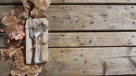 close up view of cutlery set over a napkin and autumn leaves with copy space on wooden surface