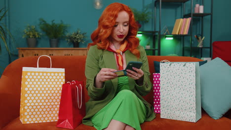 happy shopaholic redhead woman sitting with shopping bags making online payment with credit card