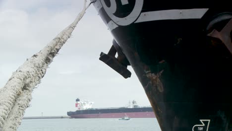 close-up bow of a big container ship tied with thick rope, harbour and boat