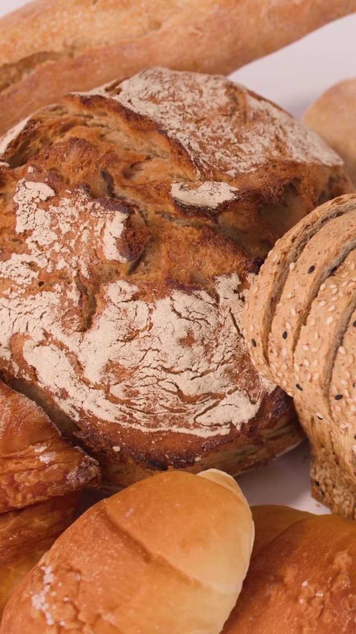 Slow zoom out reveals variety of sourdough, baguettes, and croissants with golden crusts.