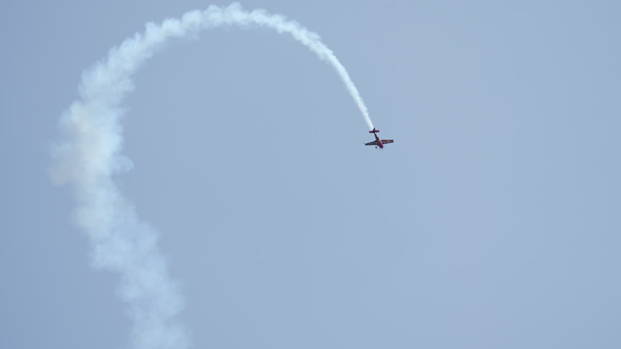 Aerobatic airplane in dramatic stunt making sharp loop while leaving thick white smoke in the sky