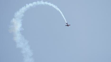 aerobatic airplane in dramatic stunt making sharp loop while leaving thick white smoke in the sky