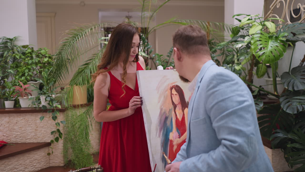 женщина смотрит на работу художника на шезлонге. красивая женщина в красном платье удивлена мастерской живописи красоты в художественном магазине. модель проверяет портретный рисунок