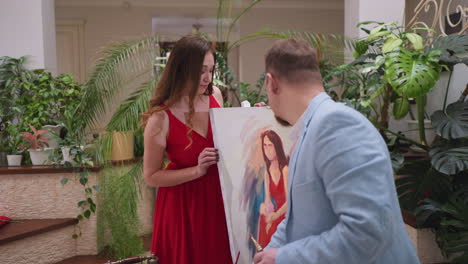 mujer mira el trabajo del artista en el caballete. hermosa mujer en vestido rojo sorprendida por la pintura maestra de la belleza en la tienda de arte. modelo comprueba el dibujo de retrato