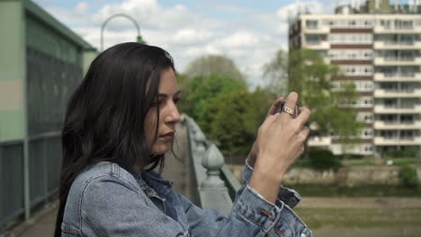 primer plano de una atractiva turista hispana tomando una foto de londres desde un puente mientras sostiene su teléfono para enmarcar la toma