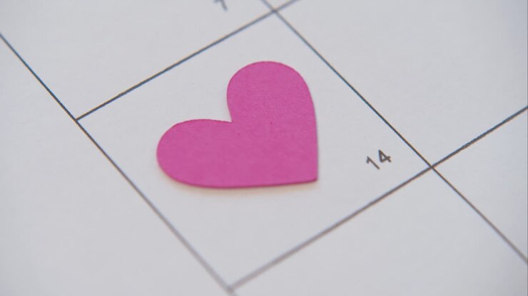 Persona che posiziona un cuore di carta sul calendario: 14 febbraio, San Valentino.