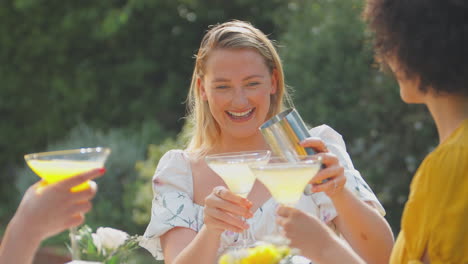 three female friends sitting outdoors in summer garden at home mixing cocktails