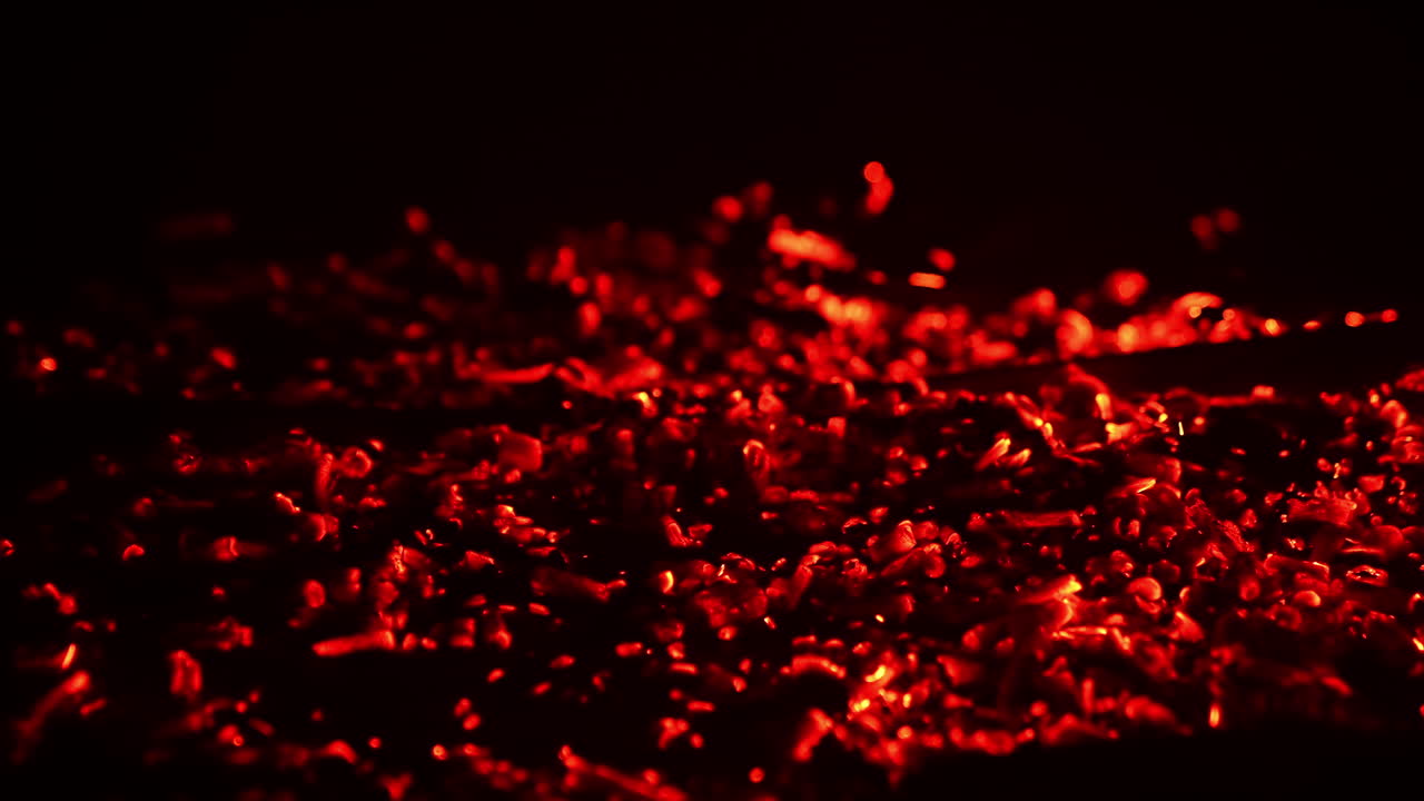 Shimmering red light appearing in the smoldering embers. Campfire burnt out and the hot pieces of charcoal flashing. Close up. Black backdrop.