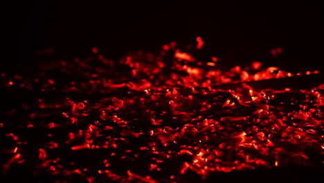 shimmering red light appearing in the smoldering embers. campfire burnt out and the hot pieces of charcoal flashing. close up. black backdrop.