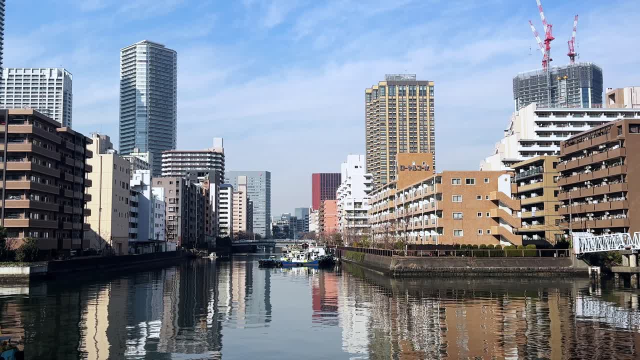 A serene view of Tokyo buildings reflecting on a calm canal under a clear blue sky