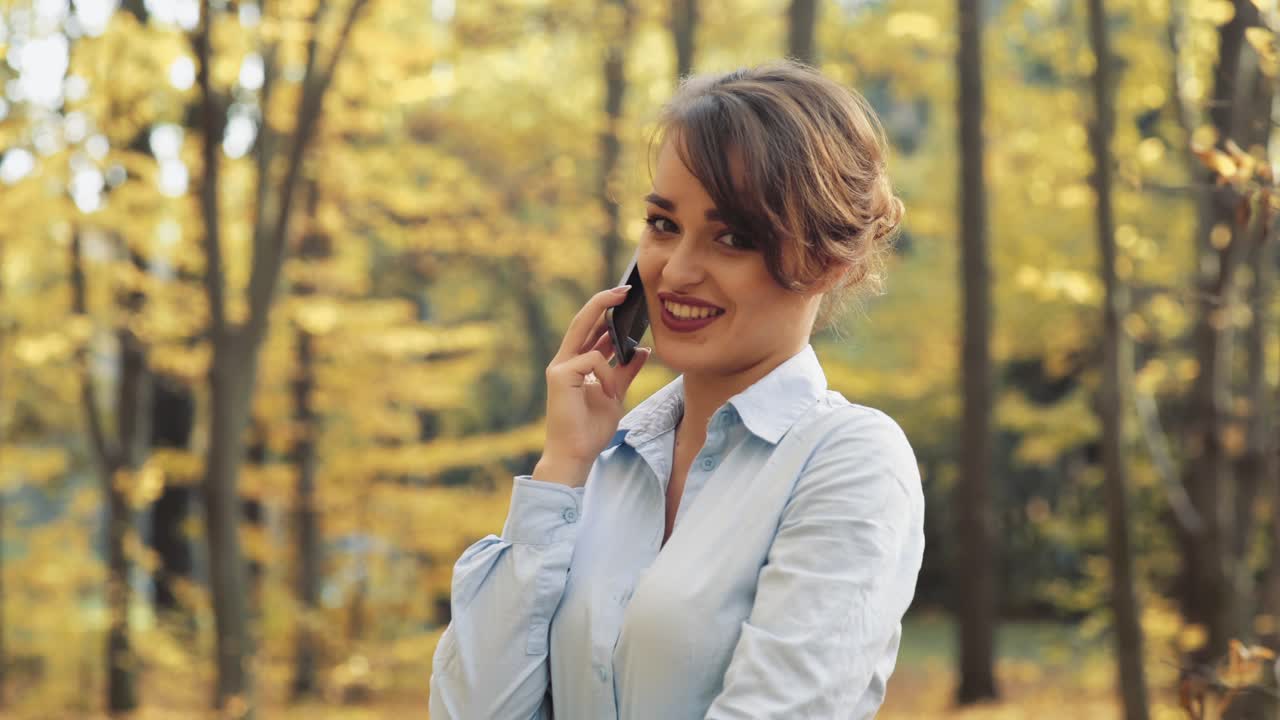 Woman with cellphone in park. Girl speaking on mobile phone in the autumn forest