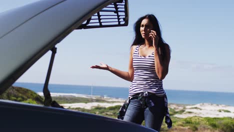 mujer afroamericana hablando en un teléfono inteligente mientras estaba de pie cerca de su coche averiado en la carretera