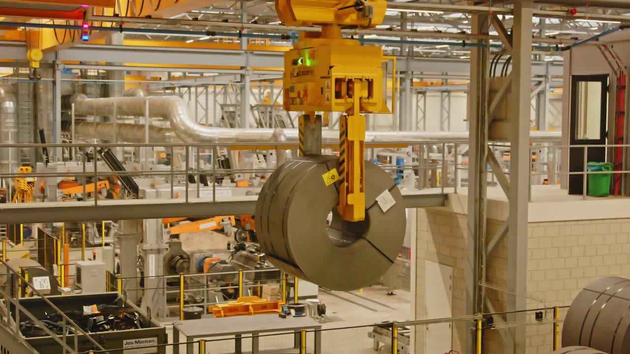 A large clamp on a crane puts down a heavy steel coil in an automated factory