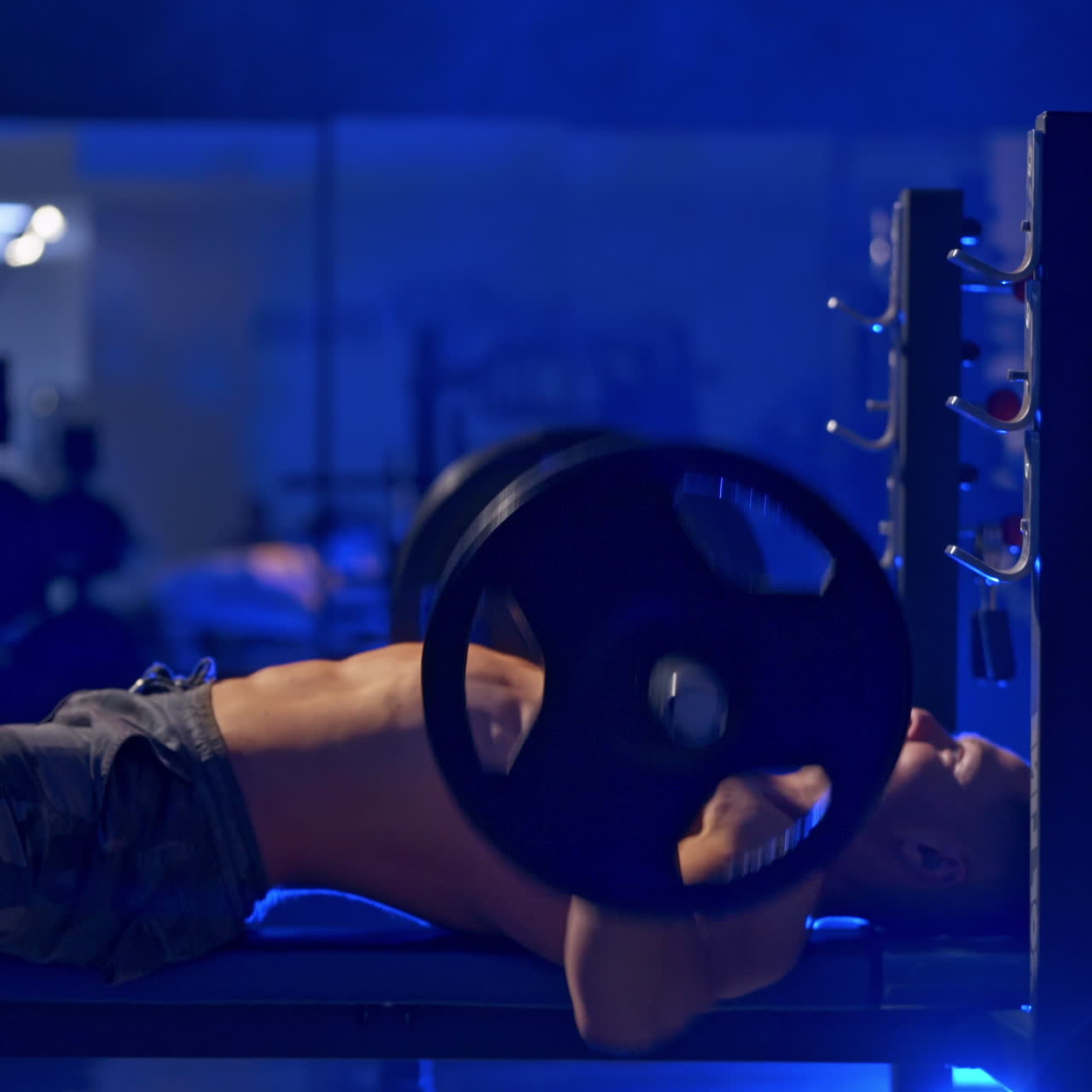 Brutal athlete with perfect body doing bench press workout in gym. Blue light filter. Video from the side.