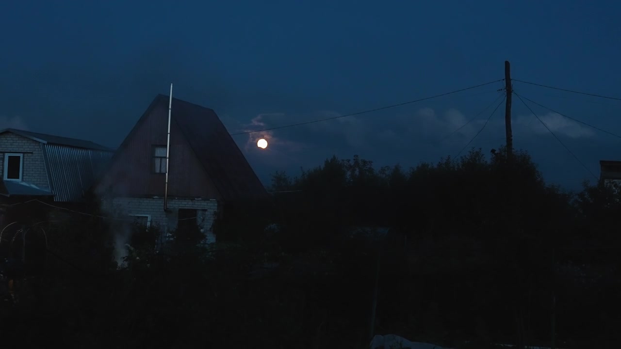 Úplněk na tmavé noční obloze nad venkovským domem s kouřem