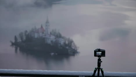 zoomed composition of lake bled island and a camera plus tripod in the foreground