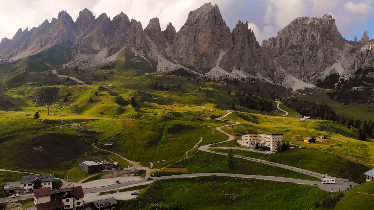 varios vehículos que se desplazan por el paso de la sella entre la hermosa pradera verde y las altas montañas de los dolomitas en el tirol del sur de italia