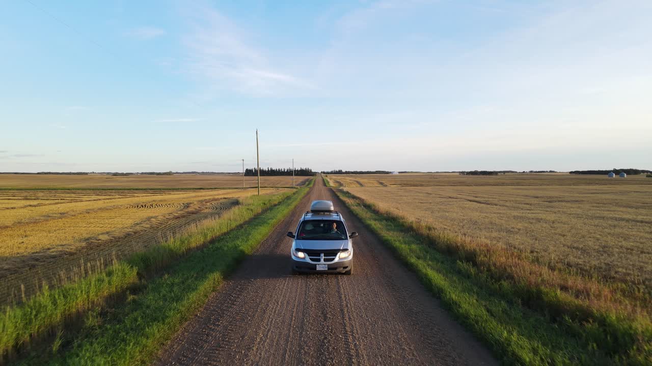 toma de seguimiento aéreo en movimiento hacia atrás de una mini furgoneta plateada que conduce a lo largo de un polvoriento camino de tierra a través del campo del centro de alberta