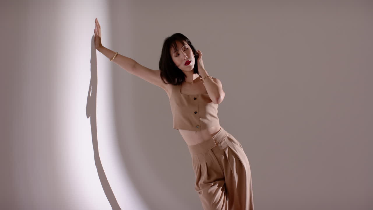 Modella cinese che appoggia la mano sinistra su una parete curva dello studio, cambiando le pose della testa durante il servizio fotografico.