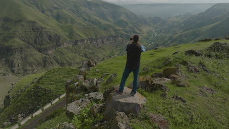 nature photographer standing on rock, taking photos of beautiful green mountains in georgia