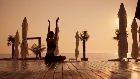 a brunette girl in a black sports summer uniform sits on a carpet on the beach, which is covered with boards, and meditates on