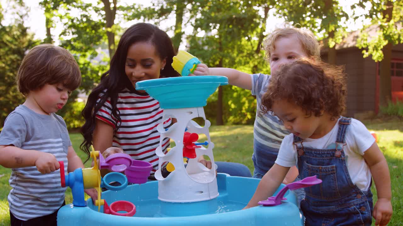 madre y niños pequeños jugando con la mesa de agua en el jardín