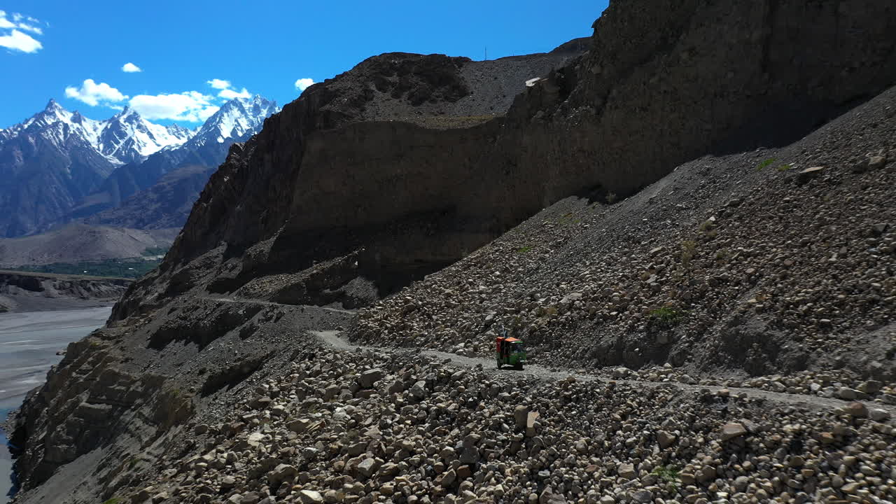 멀리 파수 콘이 있는 파키스탄 카라코람 고속도로의 자갈길에서 툭툭의 극적인 드론 샷