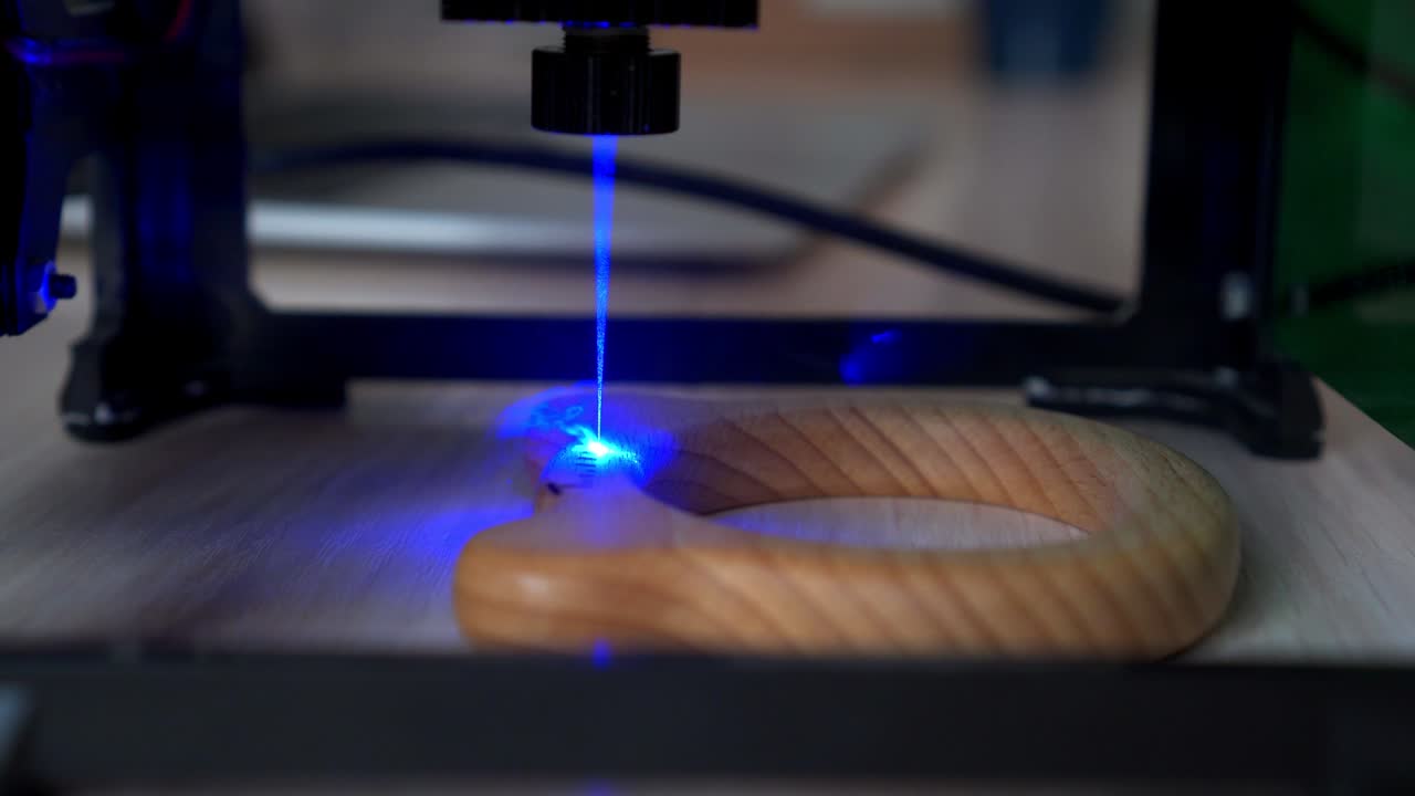 Desktop laser wood burning machine uses a blue laser beam to inscribe name on surface of childrens wooden toy. Home production of teethers and rattles for babies